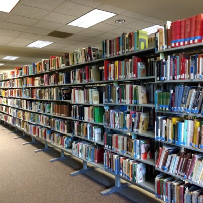 Long shelving stacks of books flagged with blue painter tape for retrieval from the Milne Library Building, Summer 2020 Some of the thousands of books flagged with blue painter tape for retrieval from the Milne Library Building, Summer 2020