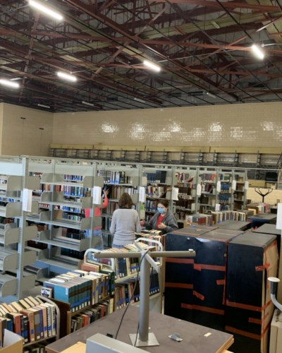 Argentieri in Schrader Hall, among shelves and long line of book trucks filled with books, Spring 2021 Argentieri in Schrader Hall, among shelves and long line of book trucks filled with books, Spring 2021